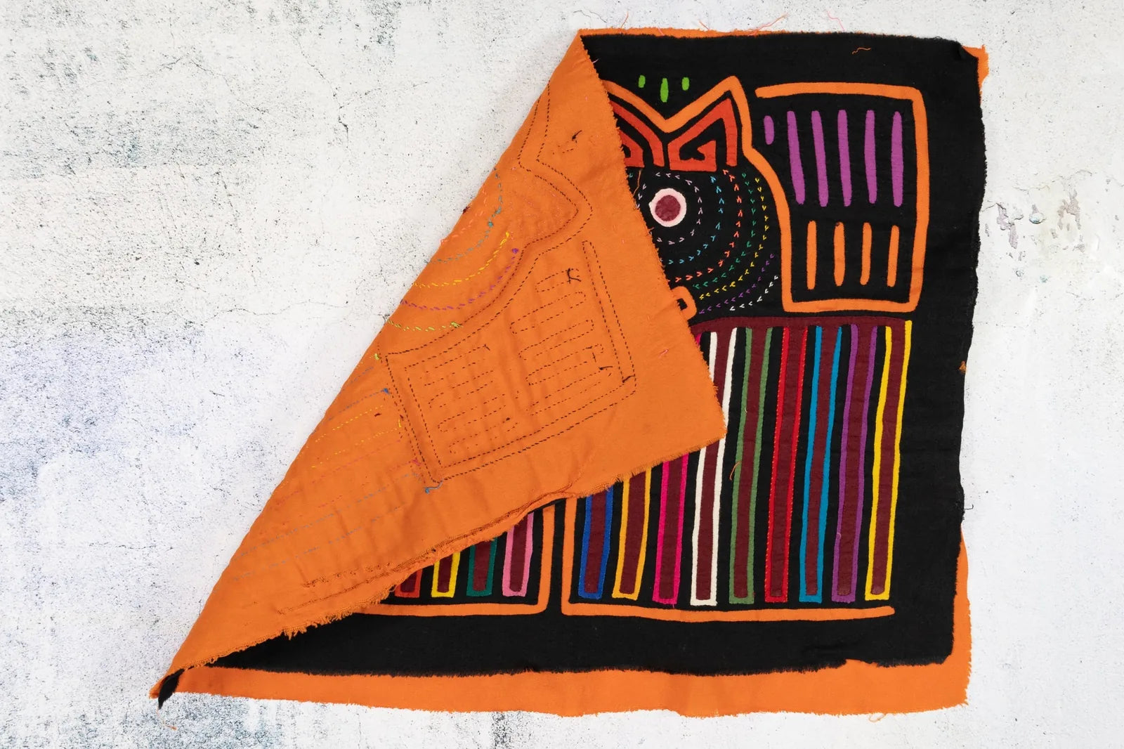 Vibrant orange and black handmade Mola tapestry featuring geometric patterns and colorful embroidered details.