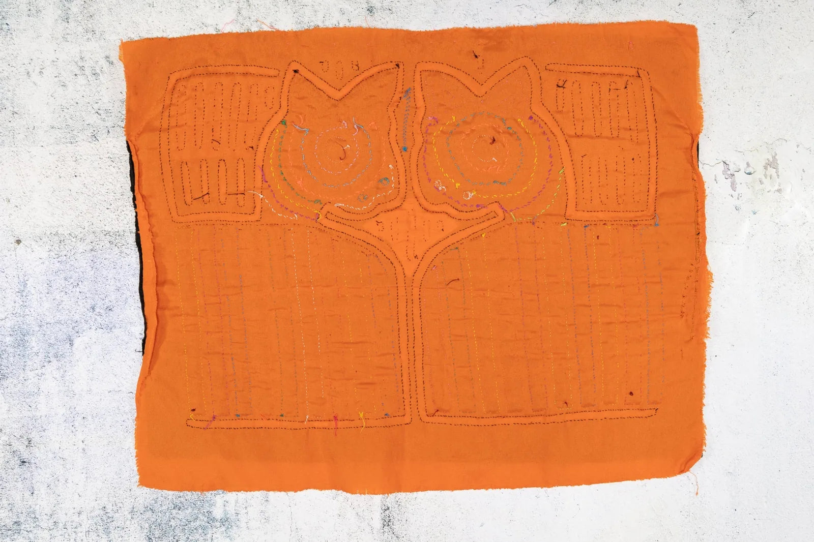 Hand-stitched orange Mola tapestry featuring two abstract dog faces with geometric designs and colorful stitching accents.