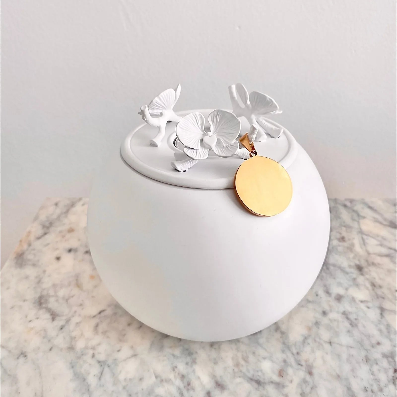 Handmade white orchid urn with a golden pendant, elegantly shaped for pet ashes, displayed on a marble surface.