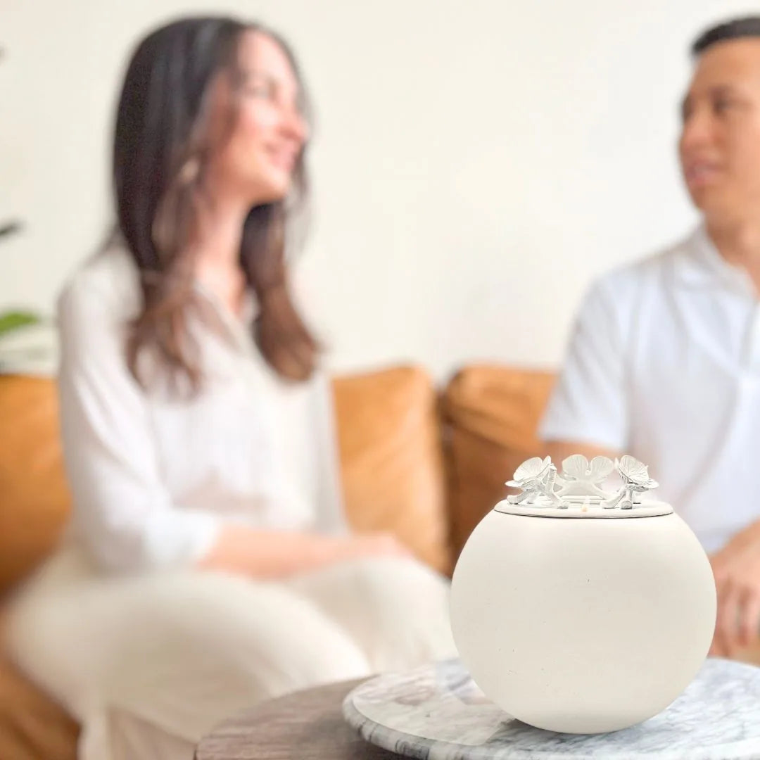 Handmade white orchid urn with a floral lid design, resting on a marble table, symbolizing pet memorial.