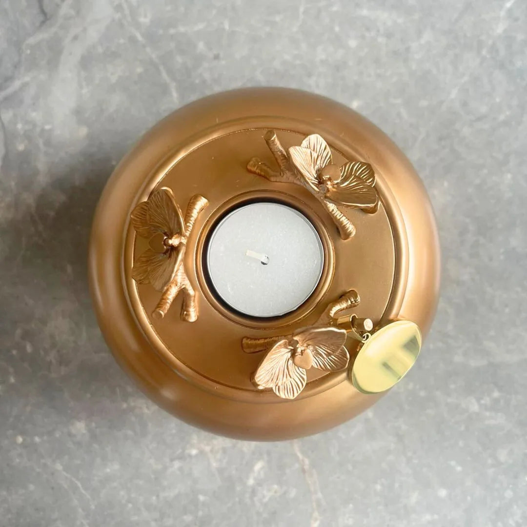 Handmade gold Orchid Urn featuring decorative floral accents and a candle holder on a smooth surface.