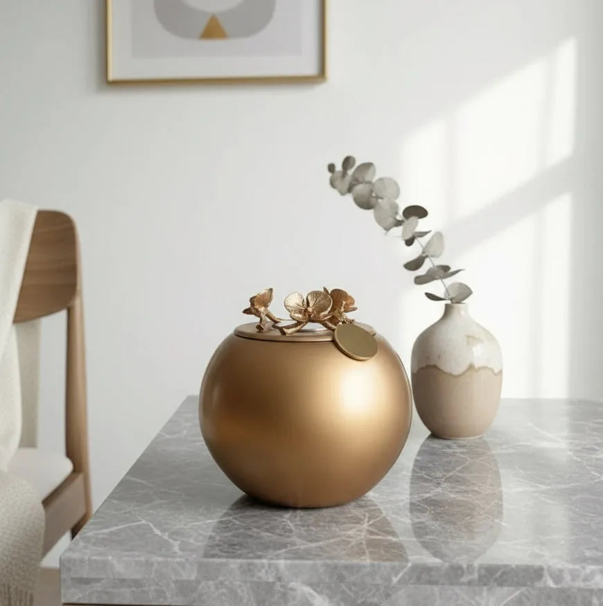 Gold Orchid Urn with floral accents resting on a marble table, surrounded by decorative vases and soft natural light.