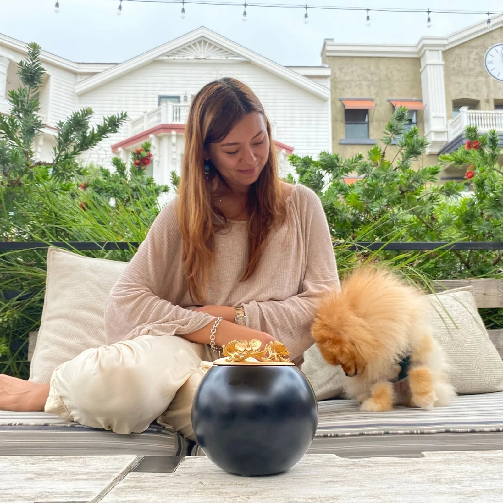 Elegant black orchid urn with gold accents, displayed beside a woman and her pet dog in a serene outdoor setting.