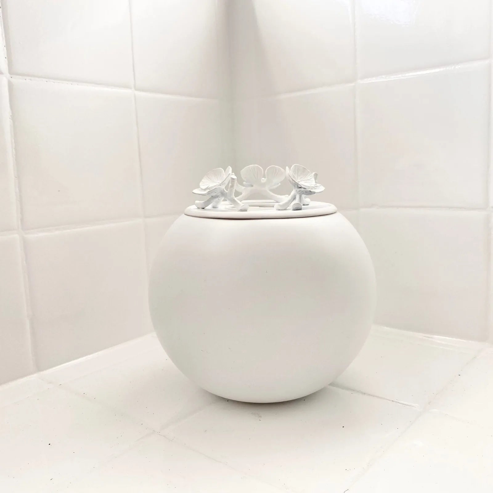 Handmade white keepsake urn with decorative butterflies on the lid, placed on a light tiled surface.