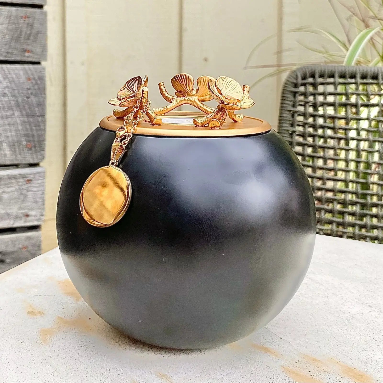 Handmade black keepsake urn with a gold floral lid and pendant, perfect for memorializing a loved one.