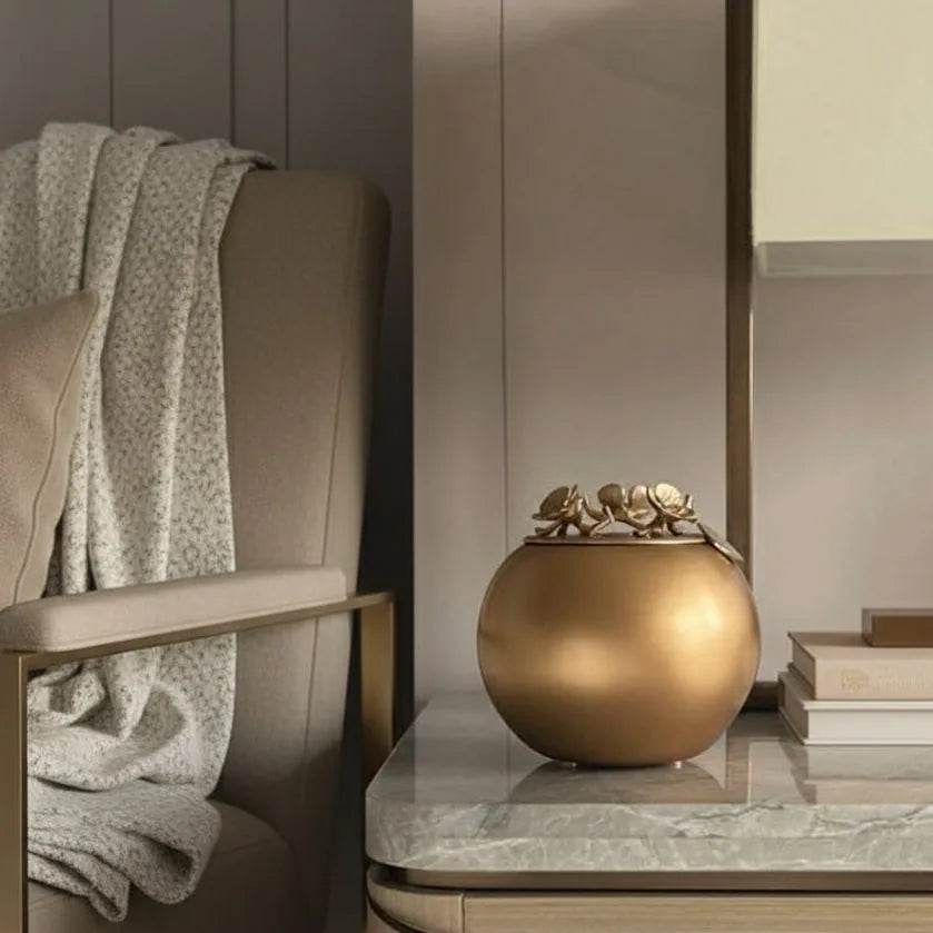 Handcrafted gold orchid urn on a marble table near a cozy chair, designed for keeping cherished memories close.