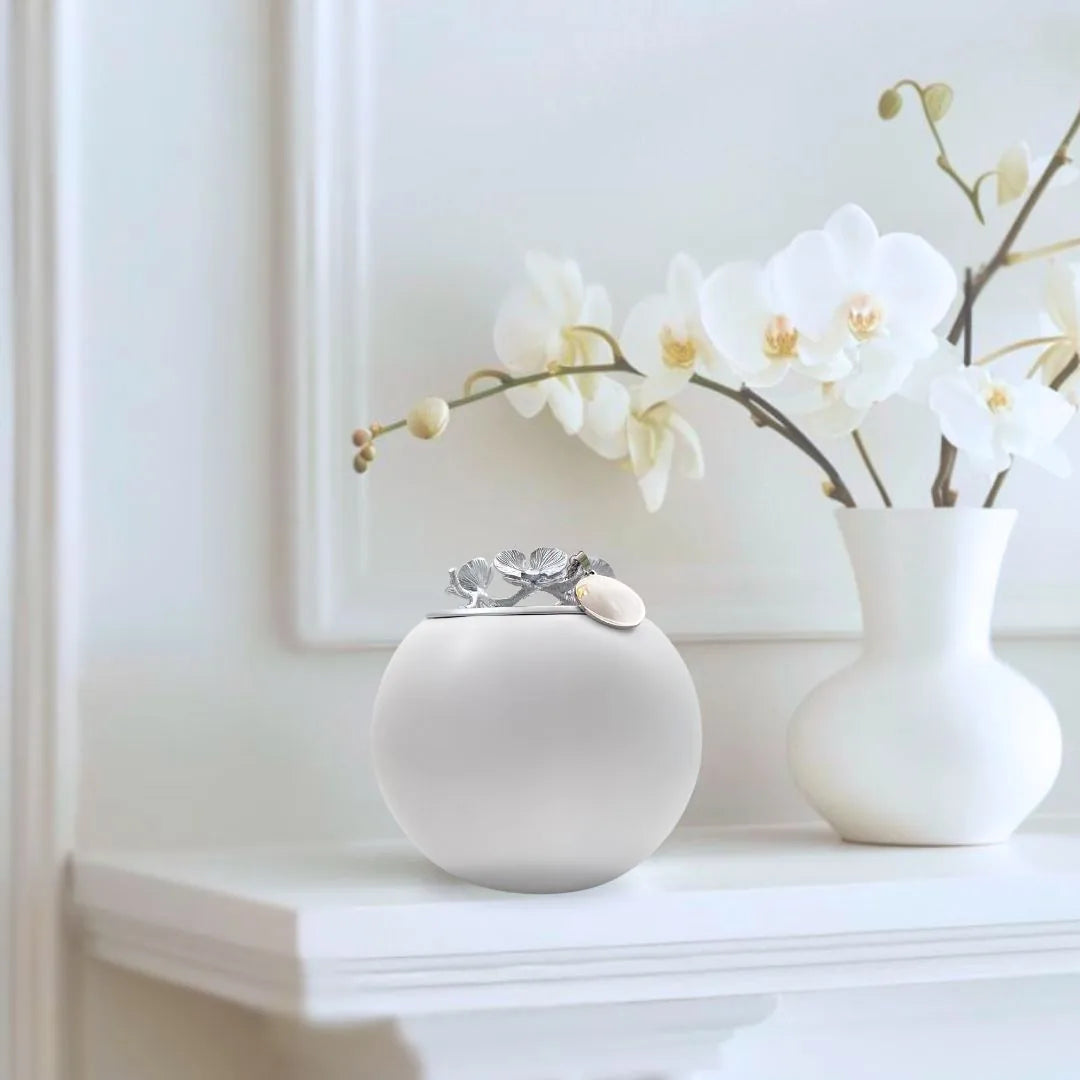 Handmade white Orchid urn with silver flower accents, elegantly displayed beside white orchids on a shelf.