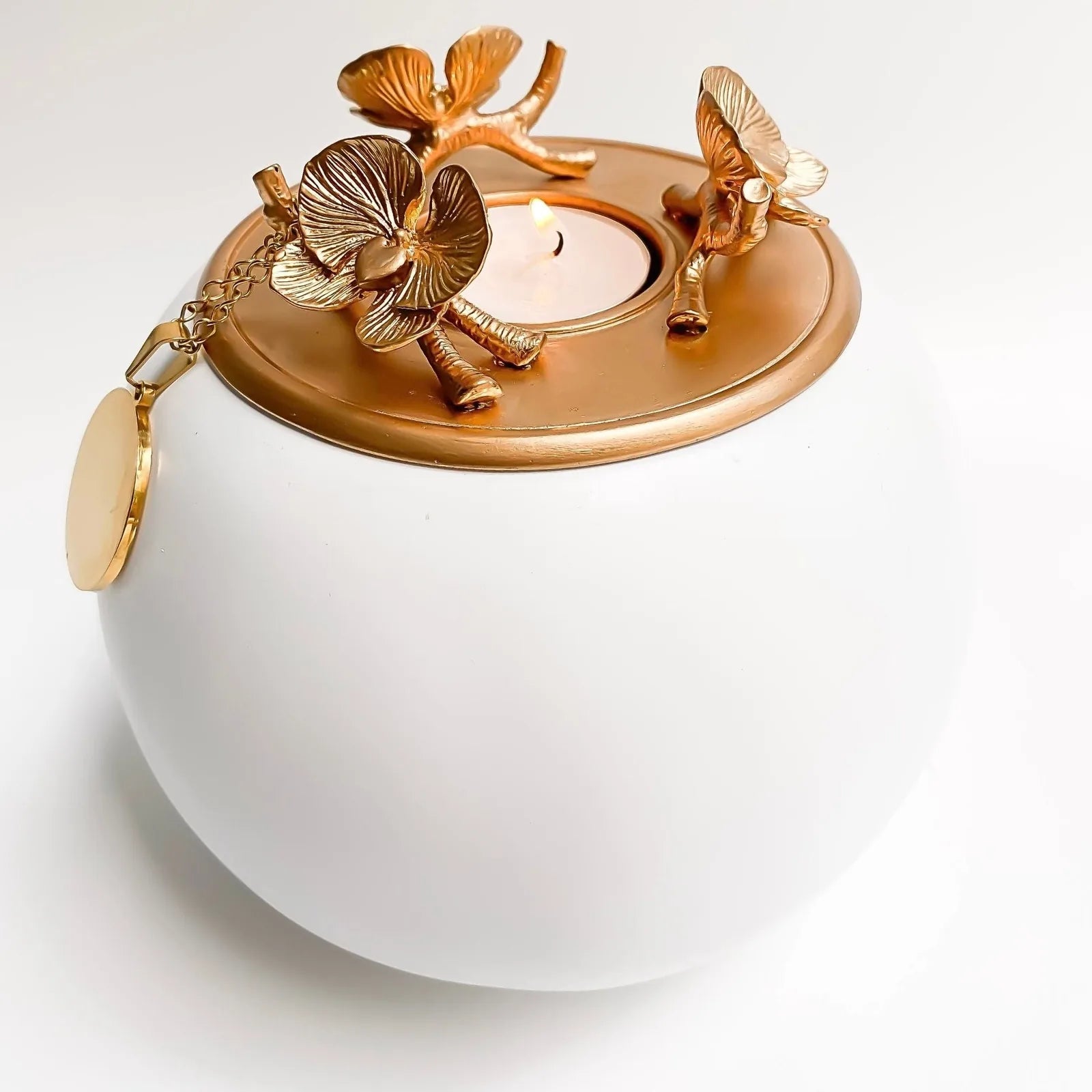 Elegant white ceramic pet urn with a gold floral lid, featuring orchids and a holder for a small candle.
