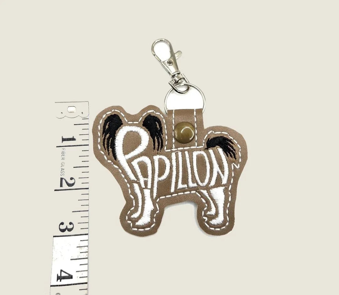 Embroidered Papillon keychain in brown felt, featuring detailed stitching and a silver-tone clasp for easy attachment.
