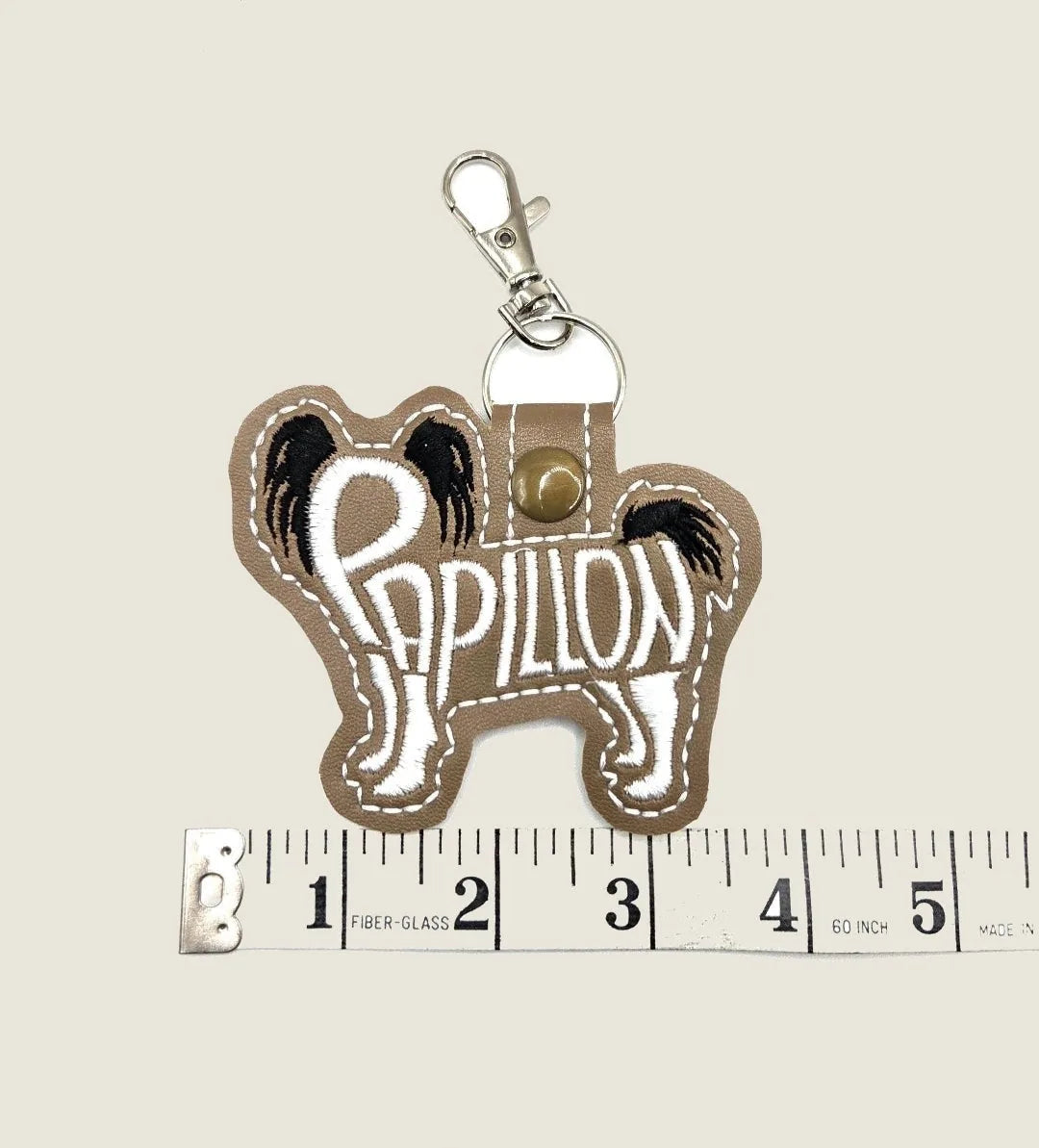 Embroidered Papillon dog keychain in brown felt, featuring white text and a silver-tone clasp for easy attachment.