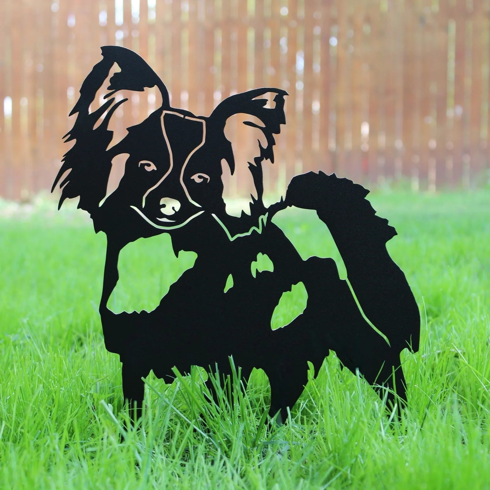 Black metal silhouette of a Papillon dog, showcasing intricate details, displayed on green grass.