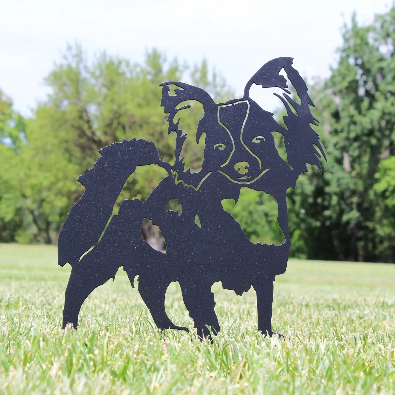 Black metal silhouette of a Papillon dog in a grassy outdoor setting, showcasing artisanal design and charm.