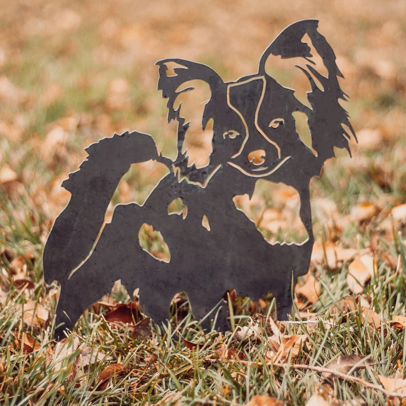 Papillon dog silhouette in Corten steel, artfully displayed on grass with fallen leaves, perfect for garden decor.