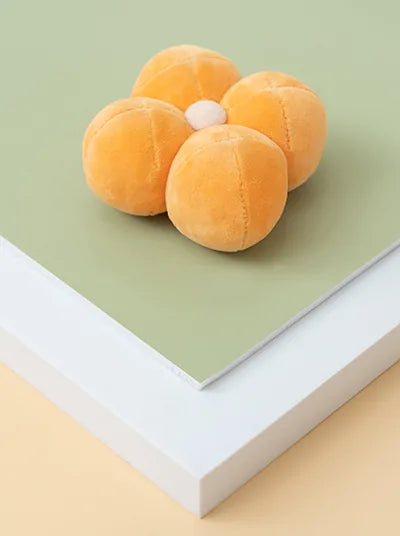 Plush orange dog toy shaped like a flower, featuring a squeaker, on soft green and white surfaces.