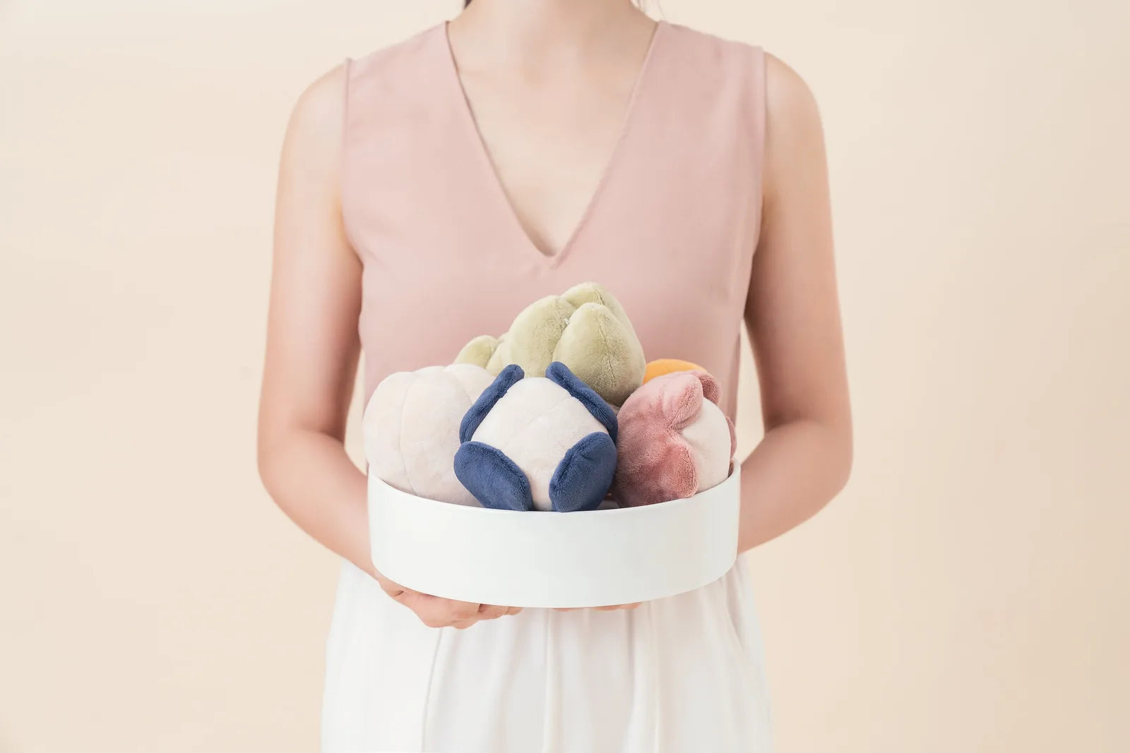 Plush dog toys in pastel colors held in a white bowl, showcasing their soft textures and playful design.