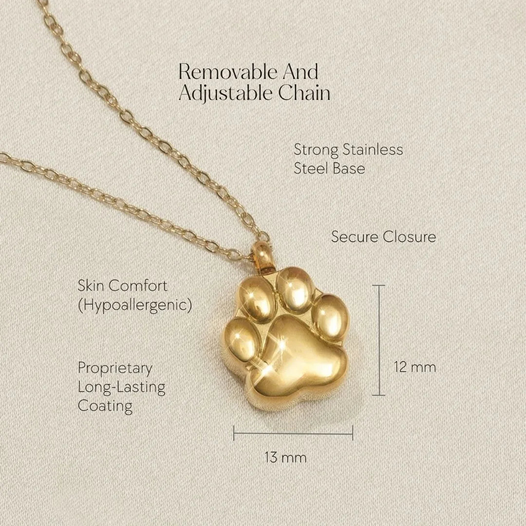 Gold paw print cremation necklace with adjustable chain, designed to hold pet ashes, set on soft fabric background.