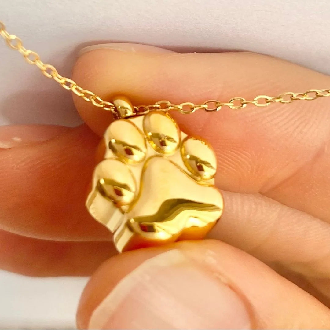 Gold paw print cremation necklace delicately held between fingers, perfect for memorializing beloved pets.