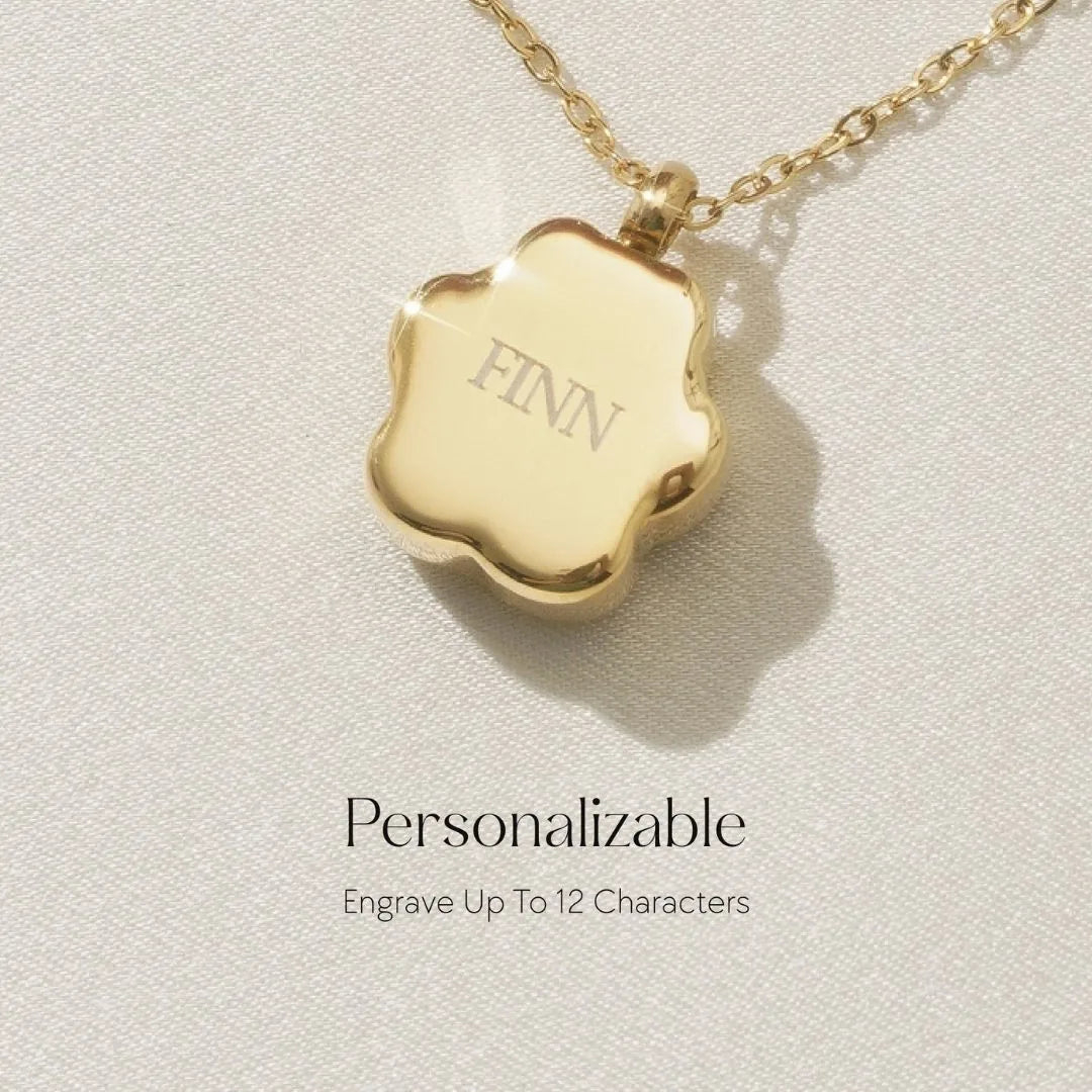 Gold paw print cremation necklace with the name "FINN" engraved, symbolizing a personal pet memorial.