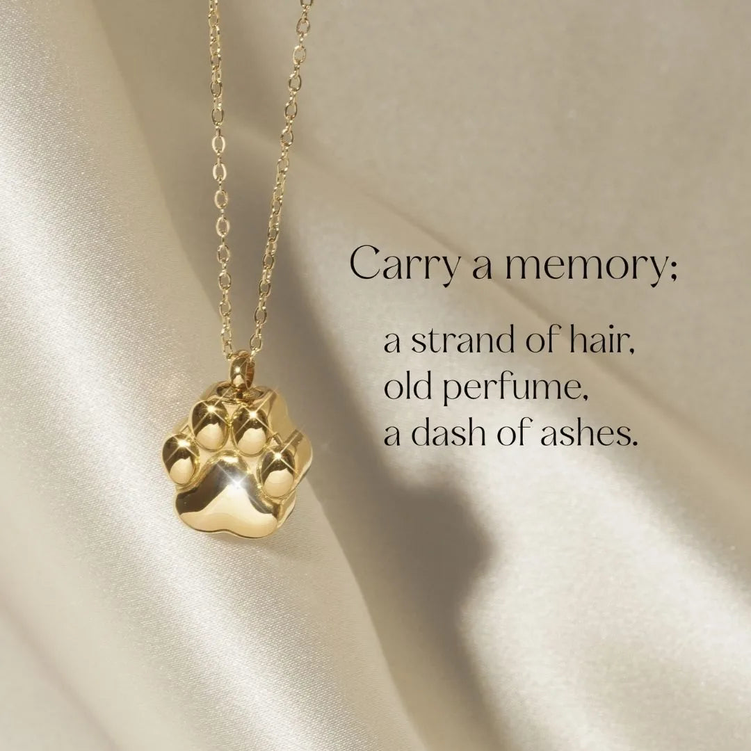 Gold paw print cremation necklace hangs on a delicate chain against a soft, light satin background.