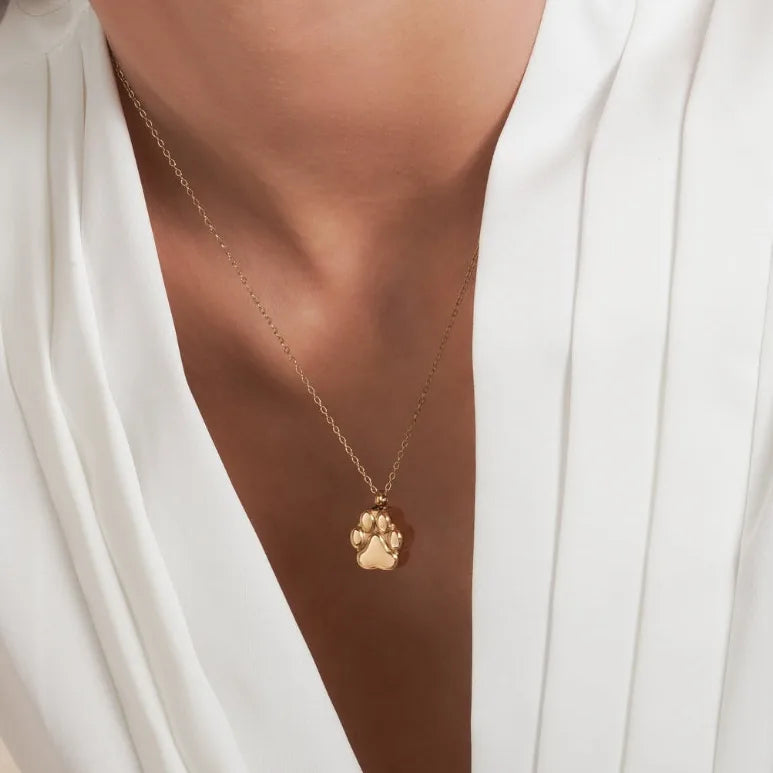 Rose gold paw print cremation necklace displayed on a model, complementing a white blouse. A heartfelt pet memorial keepsake.