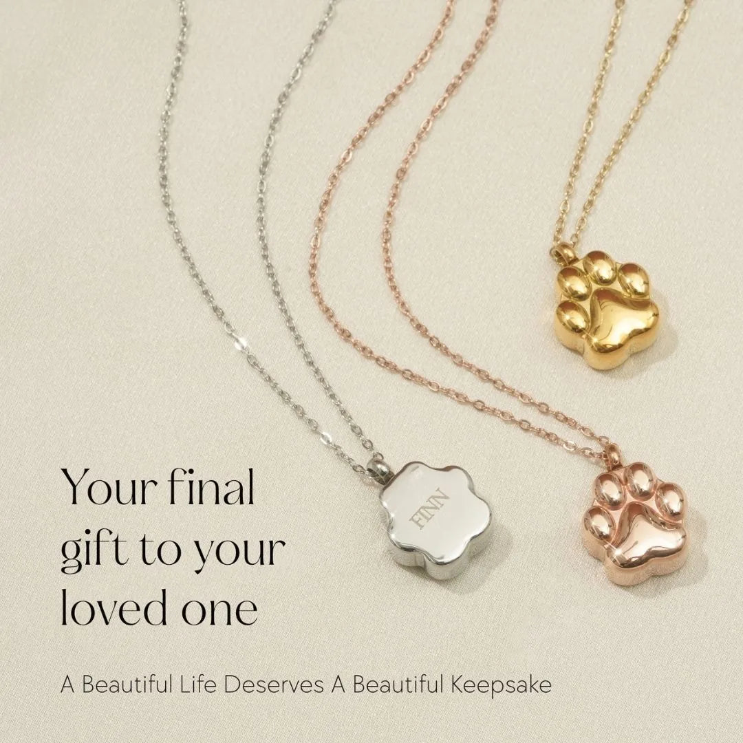 Rose gold and silver cremation necklaces with paw print designs, engraved with "FINN," displayed elegantly against a soft...