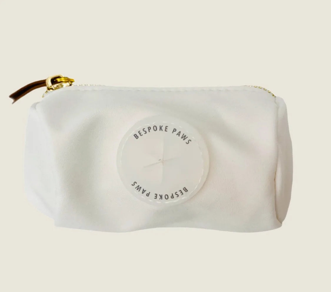 Ivory waste bag dispenser with textured surface, gold zipper, and round logo detailing from BESPOKE PAWS.