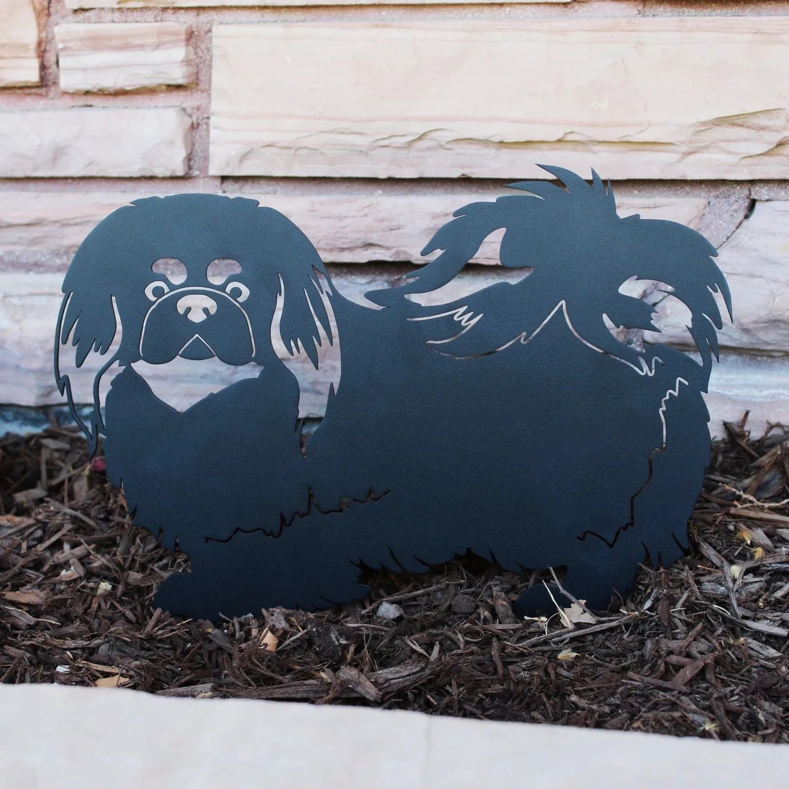 Black metal silhouette of a Pekingese dog, showcasing intricate cut-out details and positioned among mulch.