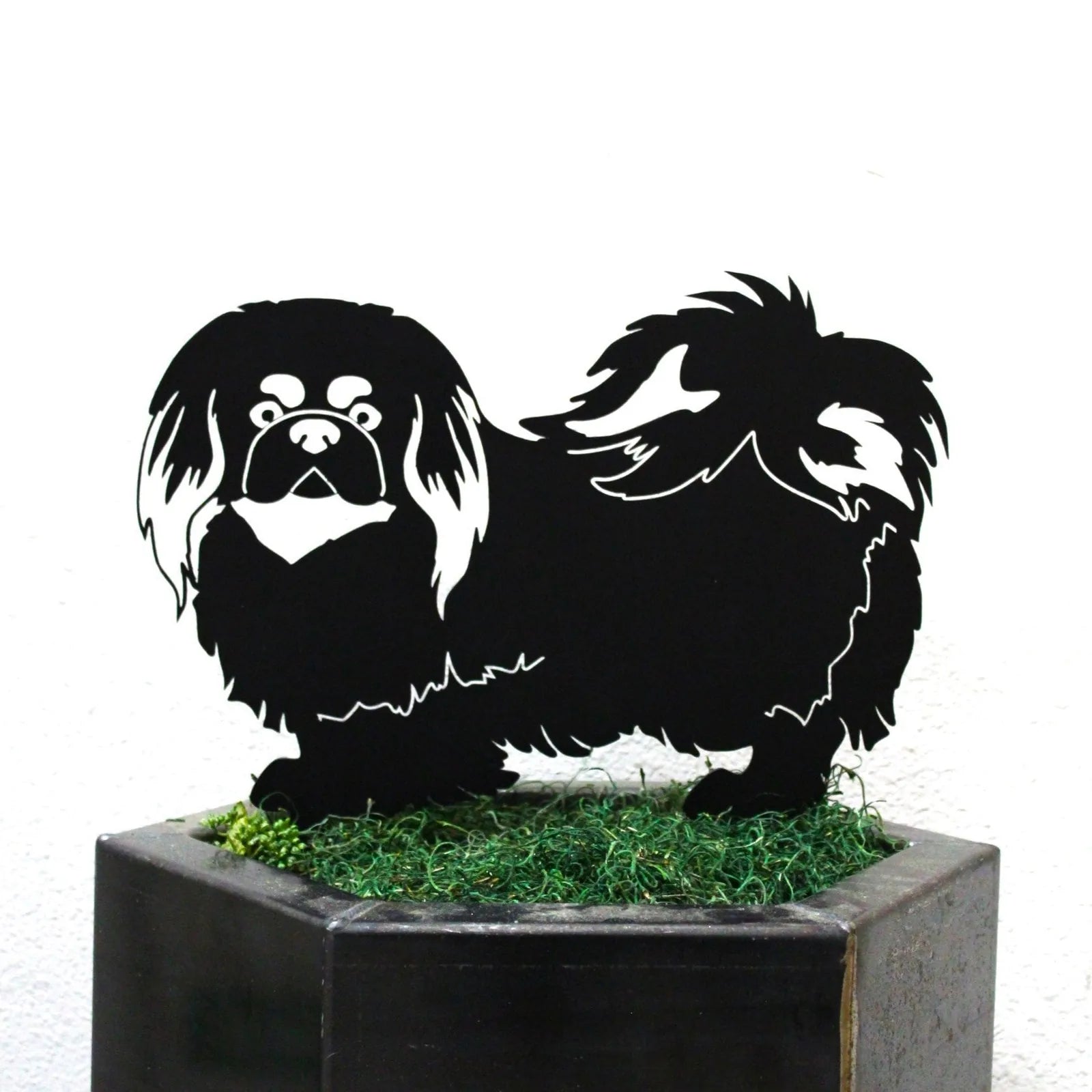 Black metal silhouette of a Pekingese dog, detailed with fur patterns, set against green faux grass.