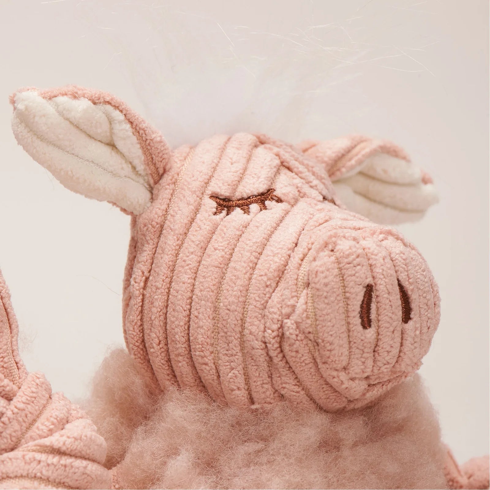 Soft pink plush pig toy with textured fabric, embroidered details, and fluffy ears, perfect for cuddling and play.