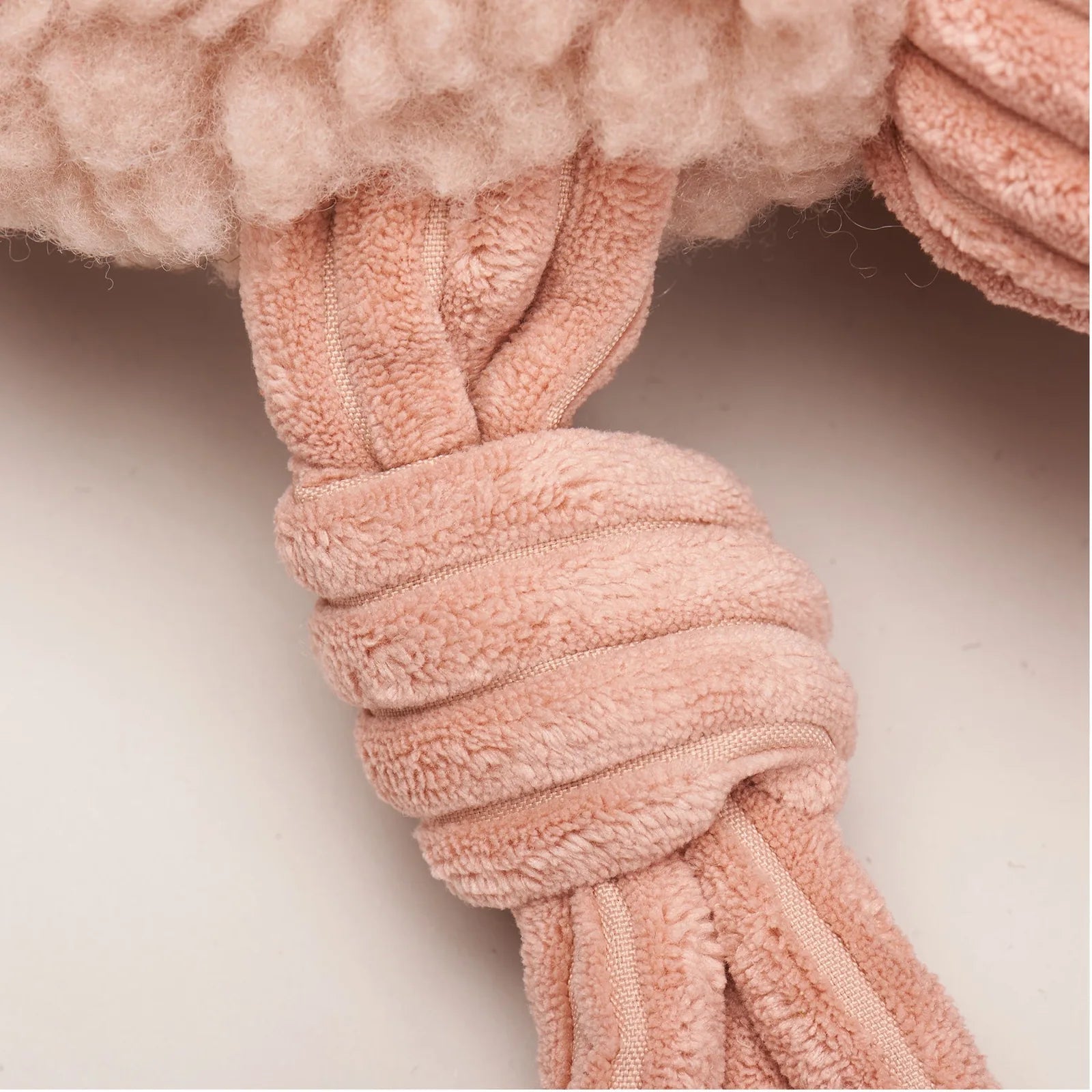 Close-up of Penelope Pig plush dog toy's textured pink fleece body and knotted, durable limbs for tugging and play.