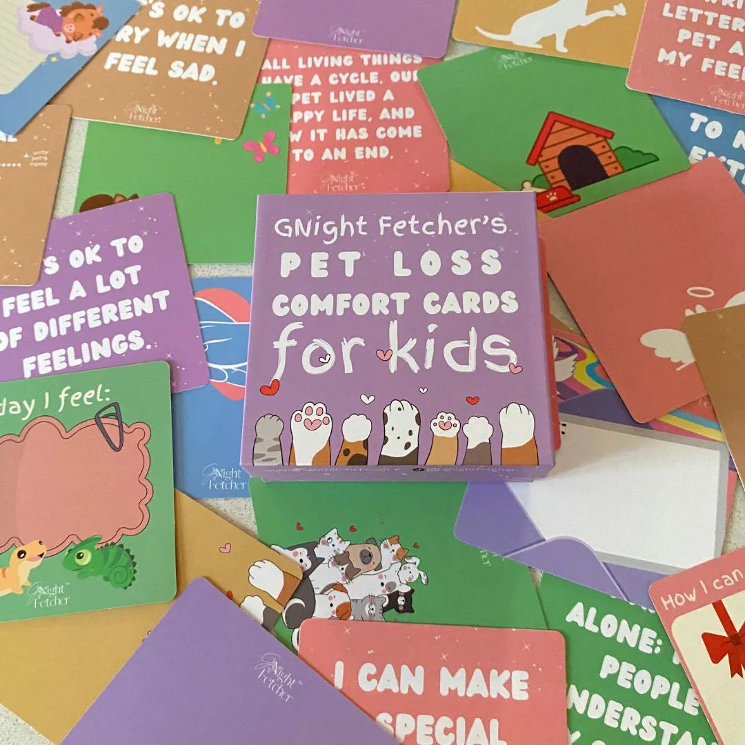 Colorful pet loss sympathy cards spread out with a purple box labeled "G'Night Fetcher's Pet Loss Comfort Cards for Kids."