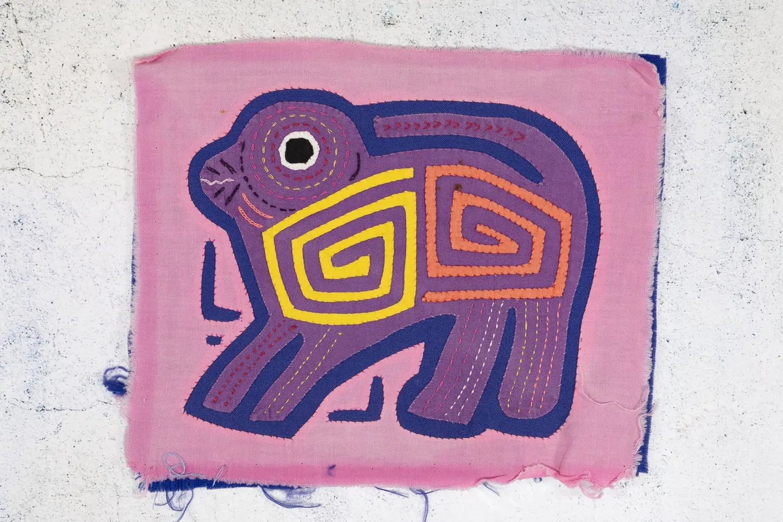 Hand-stitched pink and purple puppy dog Mola with geometric designs and vibrant colors, showcasing Panama textile art.