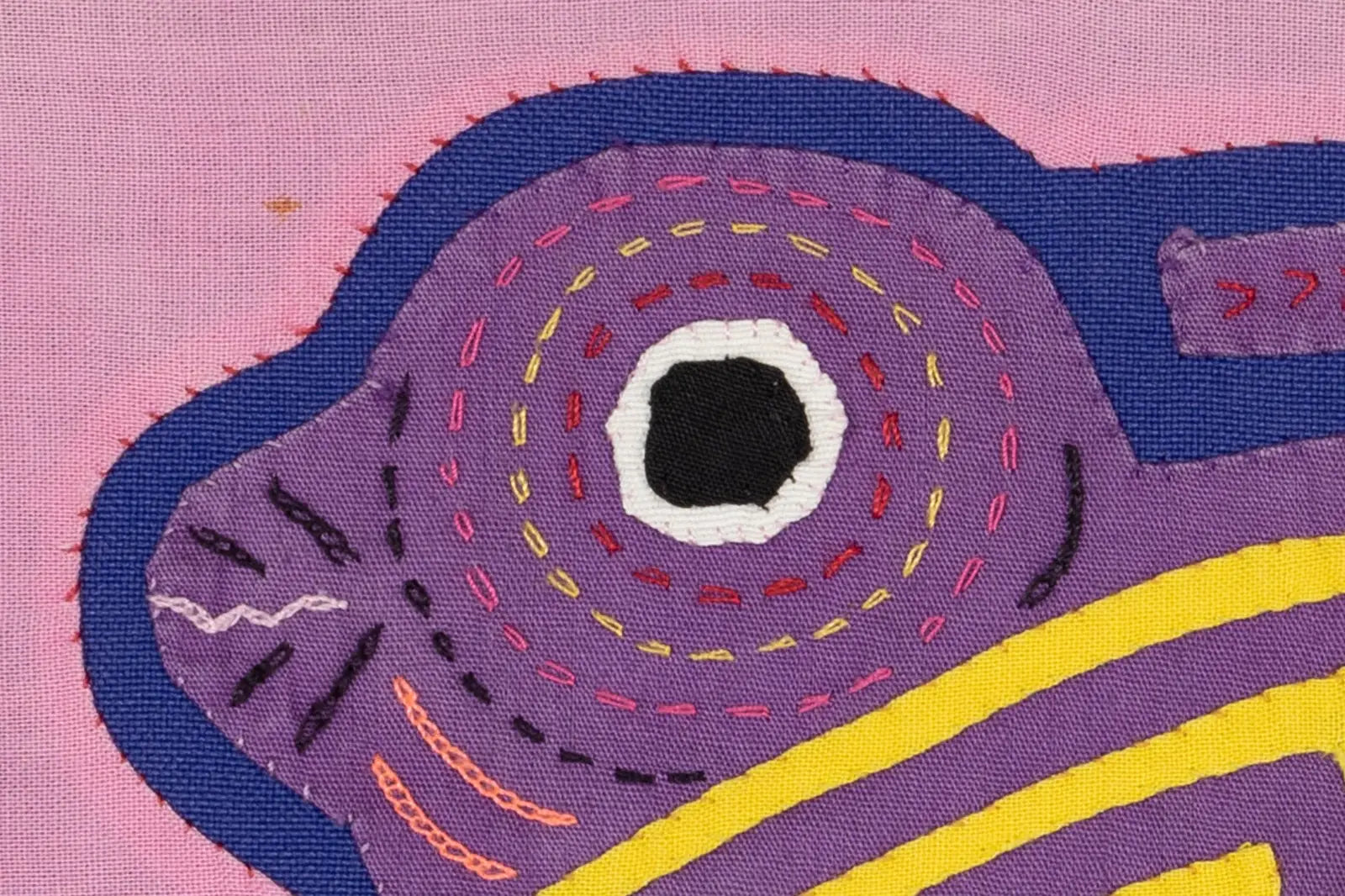 Colorful hand-stitched Molita featuring a purple and pink design with intricate patterns and textures on a textile backgro...