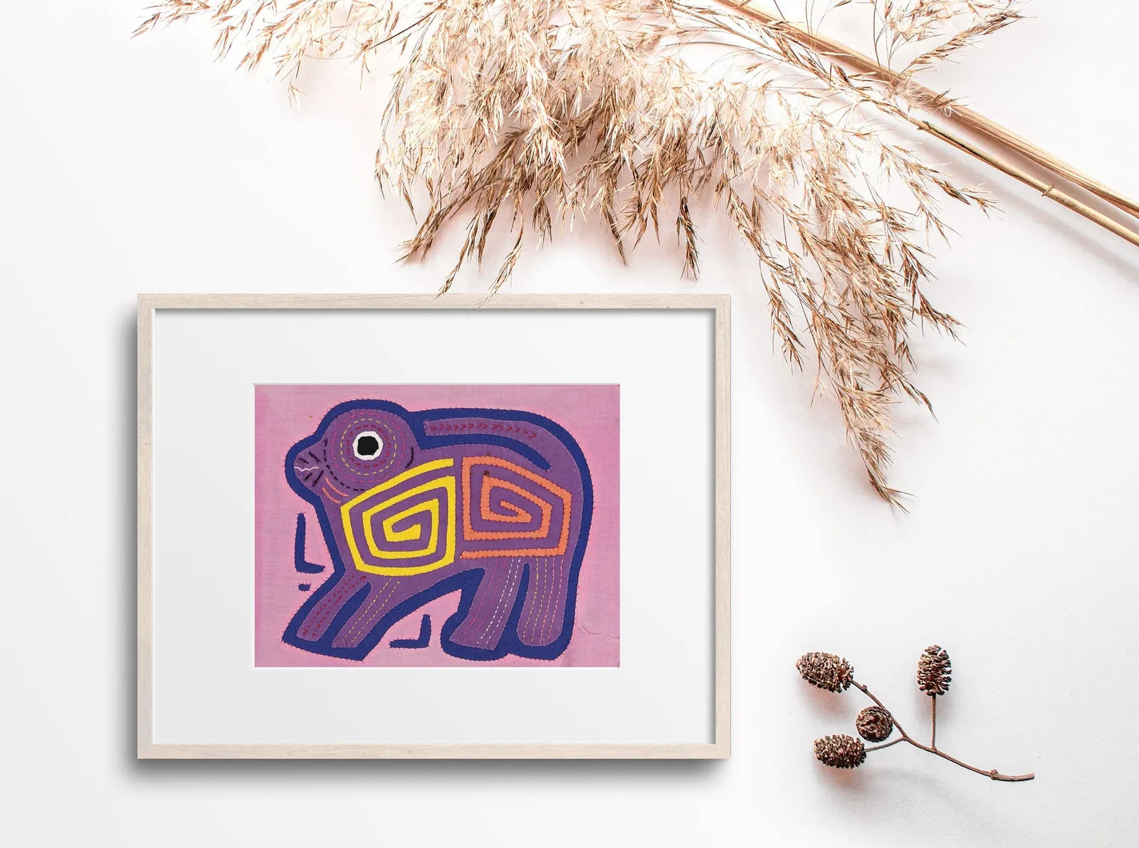 Hand-stitched pink and purple puppy dog Molita tapestry with geometric patterns, framed in light wood.