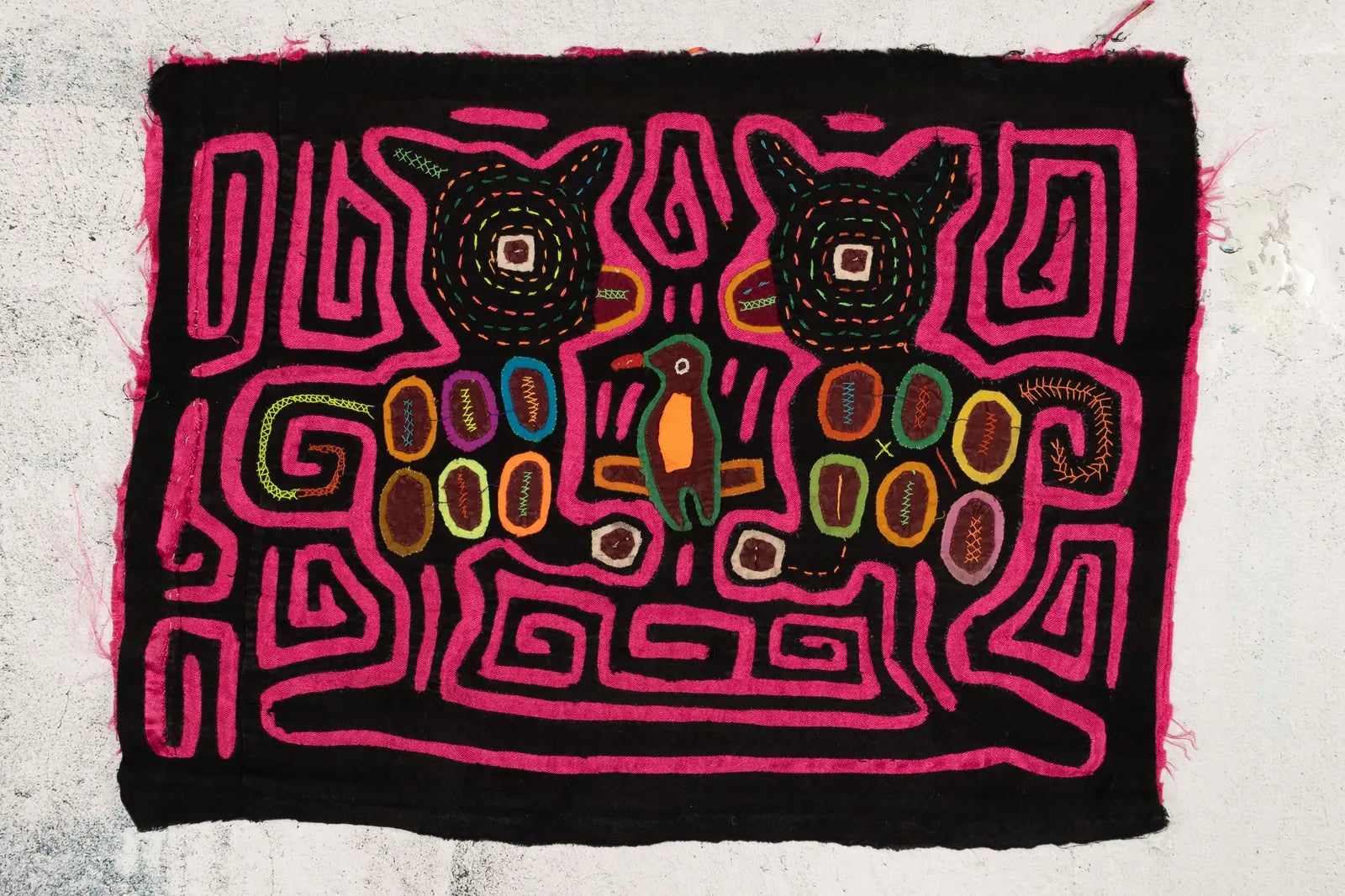 Colorful hand-stitched Mola featuring geometric patterns, wildlife motifs, and vibrant pink, black, and earthy tones.