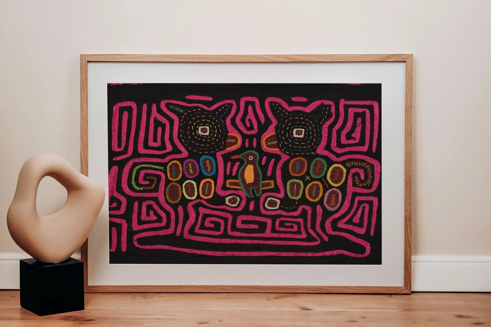 Hand-stitched pink Mola with geometric dog designs, featuring vibrant colors on a dark background, framed and displayed.