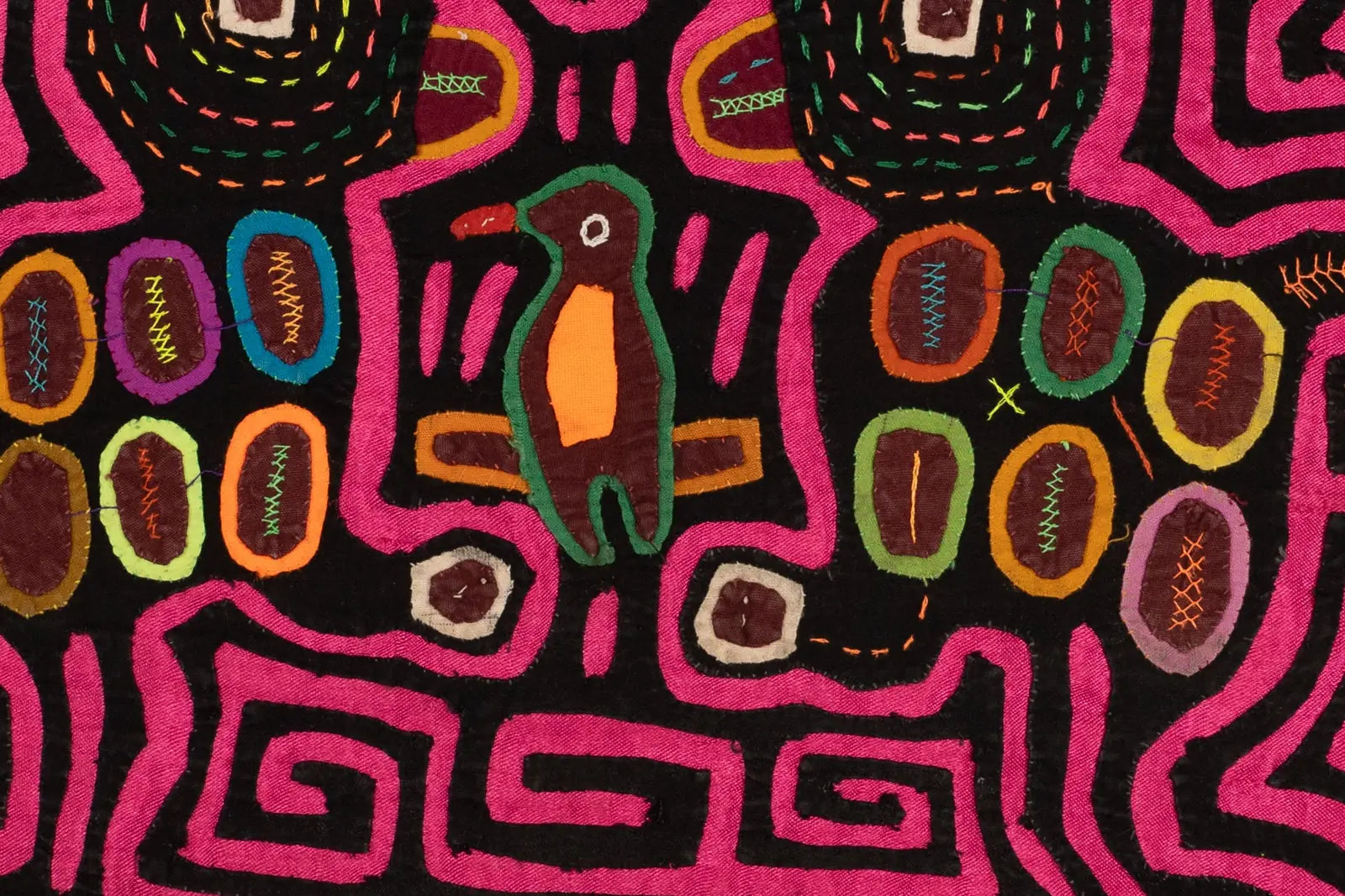 Colorful hand-stitched Mola featuring a green and orange bird design on a black background with vibrant pink and geometric...
