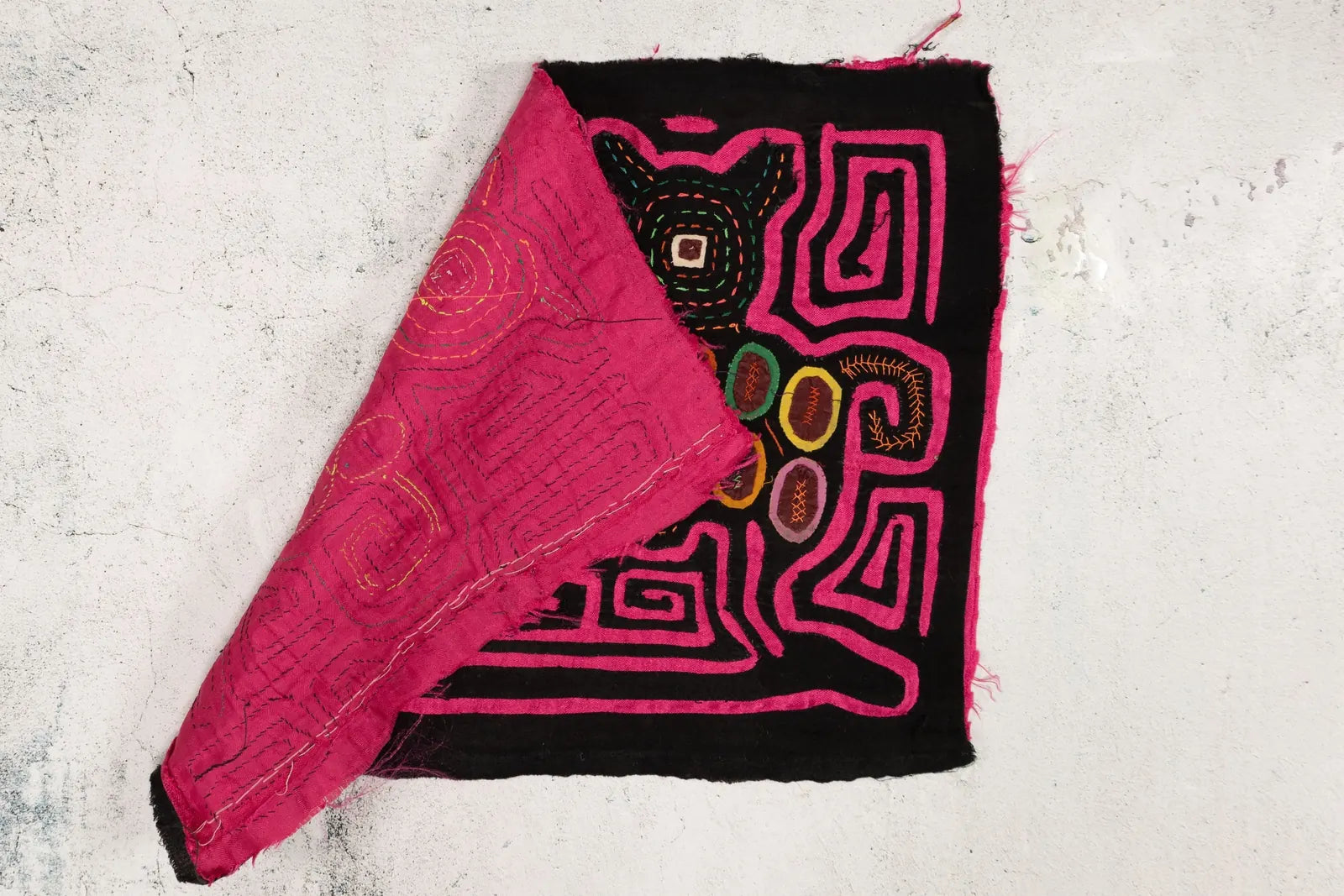 Hand-stitched pink and black Mola with geometric designs, showcasing vibrant colored patterns inspired by nature.