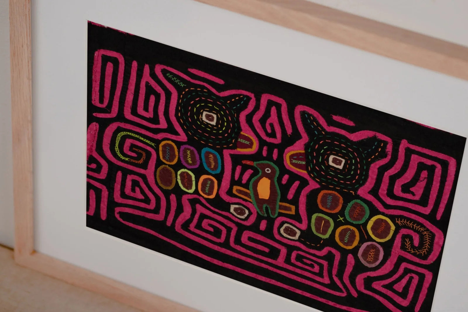 Hand-stitched pink Mola tapestry featuring geometric animal designs on a black background. Unique textile art from Panama.