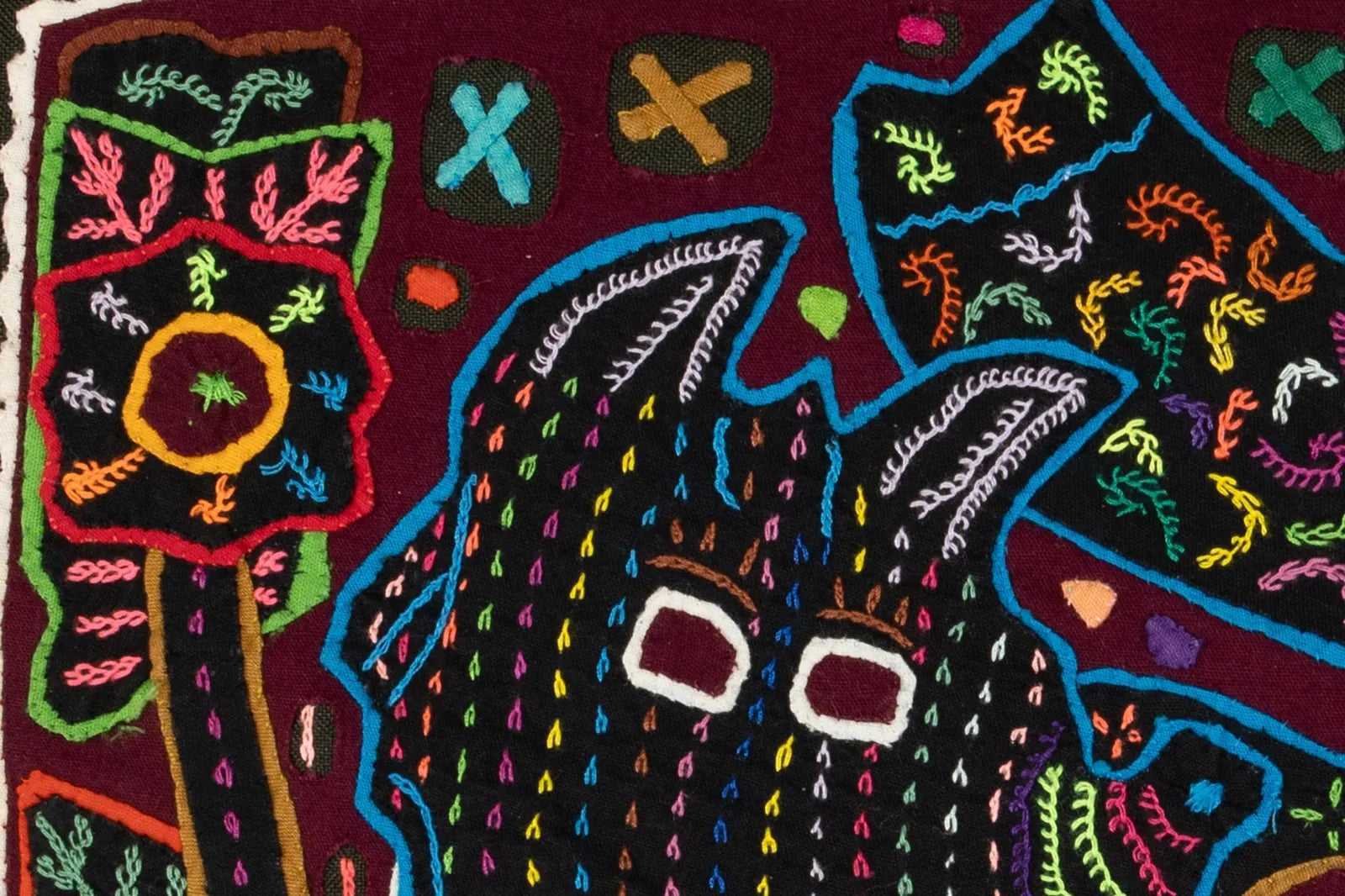Colorful hand-stitched mola featuring a playful terrier puppy with geometric patterns on a maroon background.
