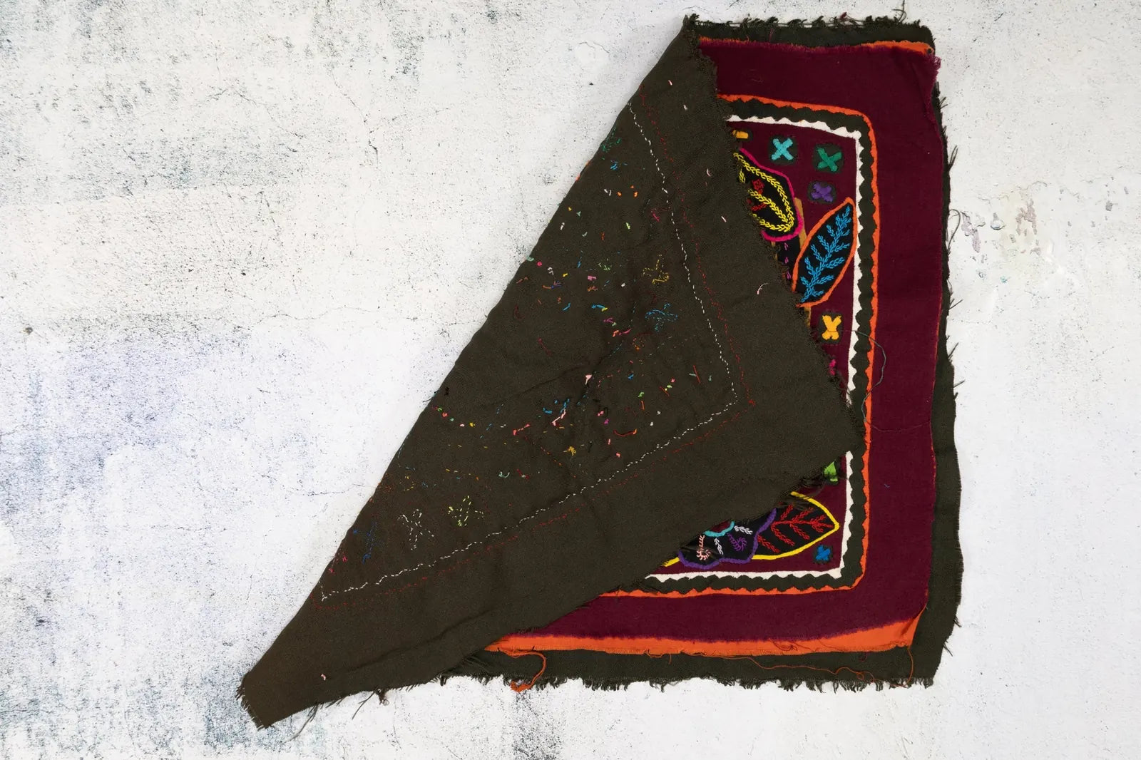 Colorful hand-stitched Mola textile featuring geometric patterns and vibrant leaves on a dark background.