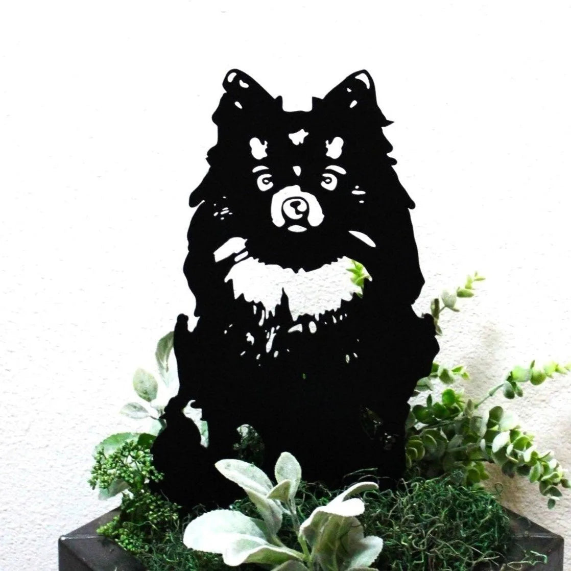 Black metal Pomeranian silhouette poised among green foliage, showcasing detailed fur and facial features for outdoor decor.