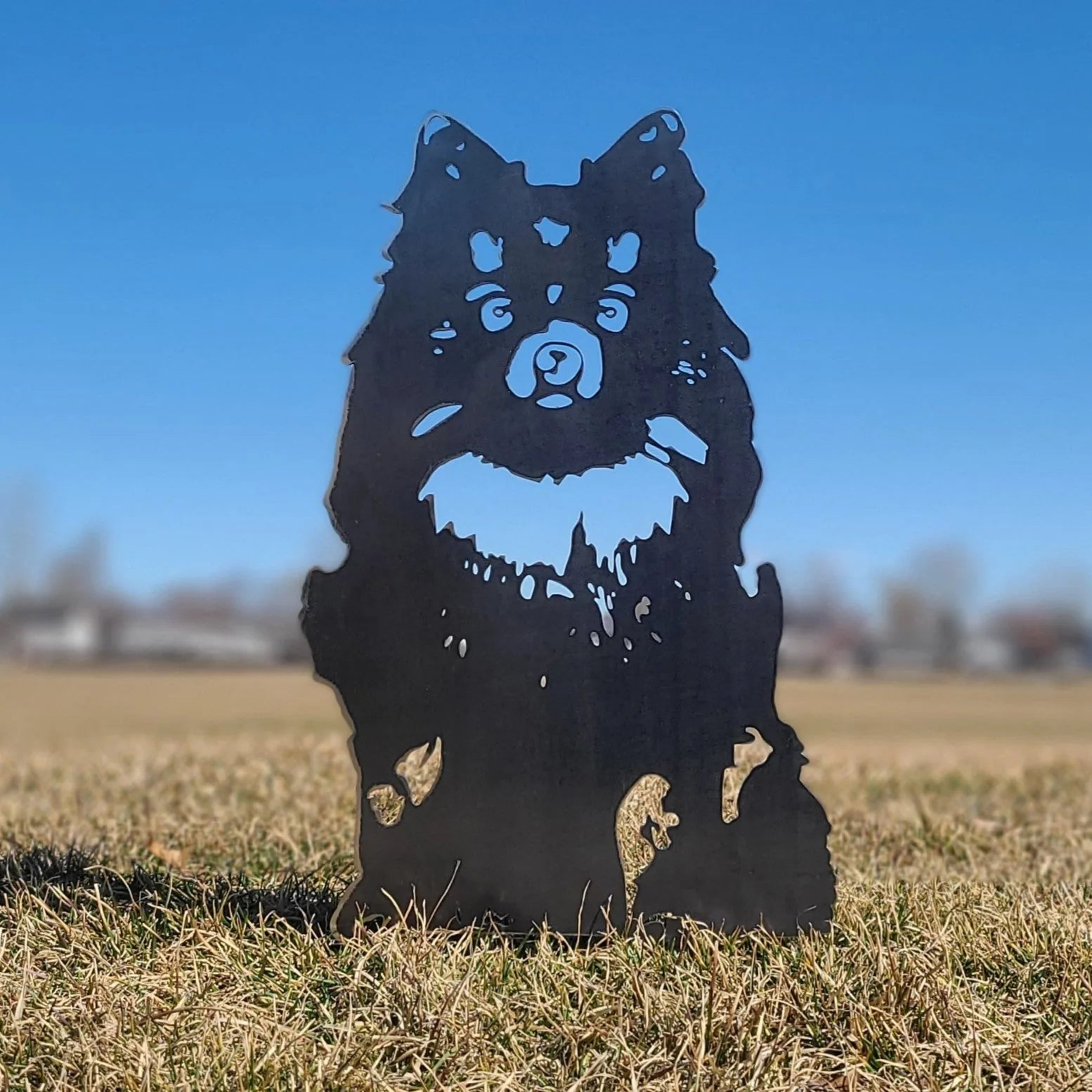 Black metal silhouette of a Pomeranian dog standing on grass against a clear blue sky, crafted from sturdy material.
