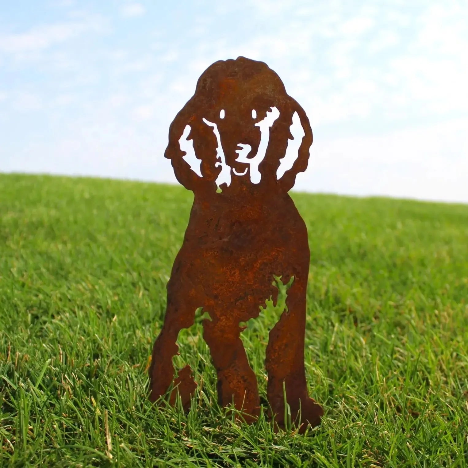 Rusty metal silhouette of a poodle dog standing in green grass, designed for outdoor decor.