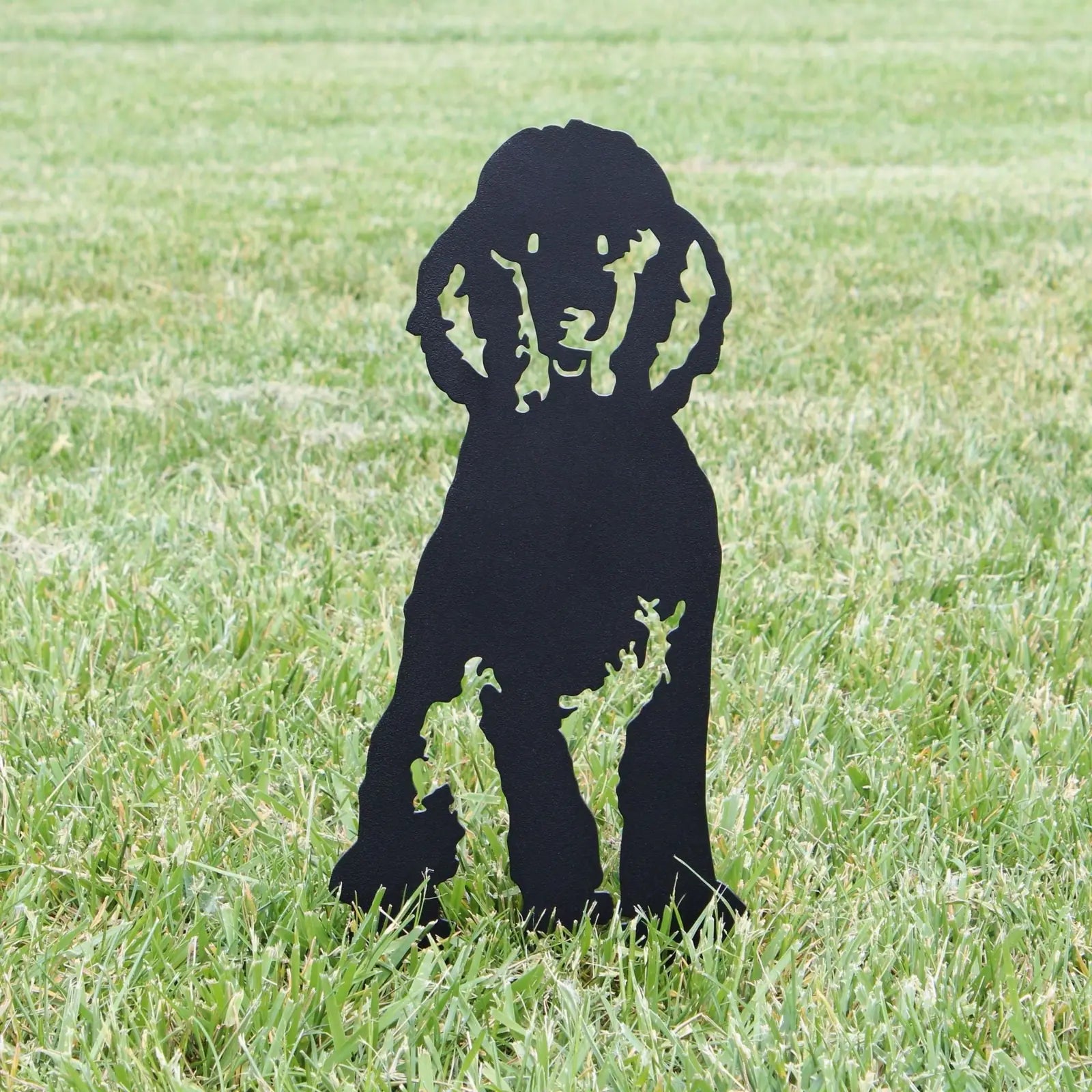 Black metal silhouette of a poodle dog standing on lush green grass, perfect for outdoor decor.