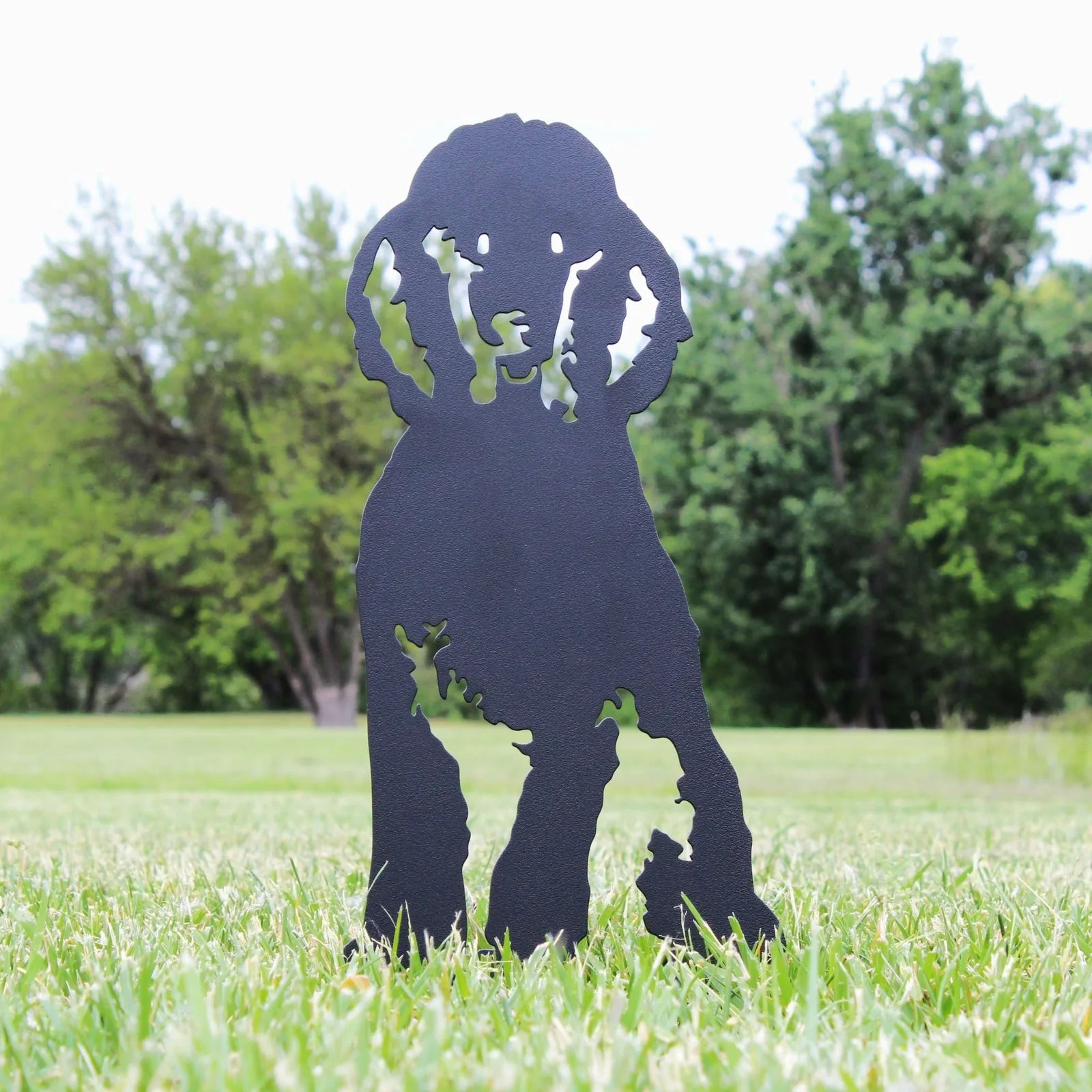 Black metal silhouette of a poodle standing in a grassy outdoor setting, perfect for garden decor.