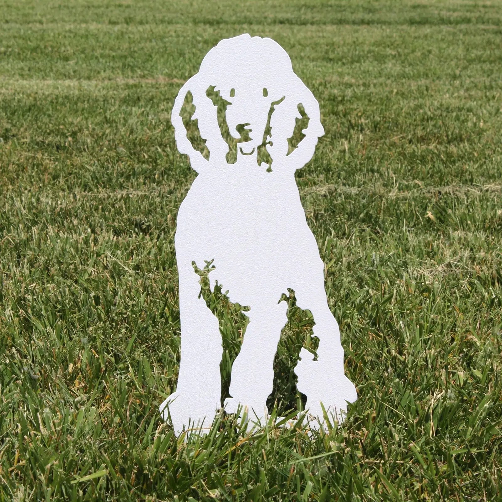 White metal silhouette of a poodle dog standing on grass, designed for outdoor decor and yard decoration.