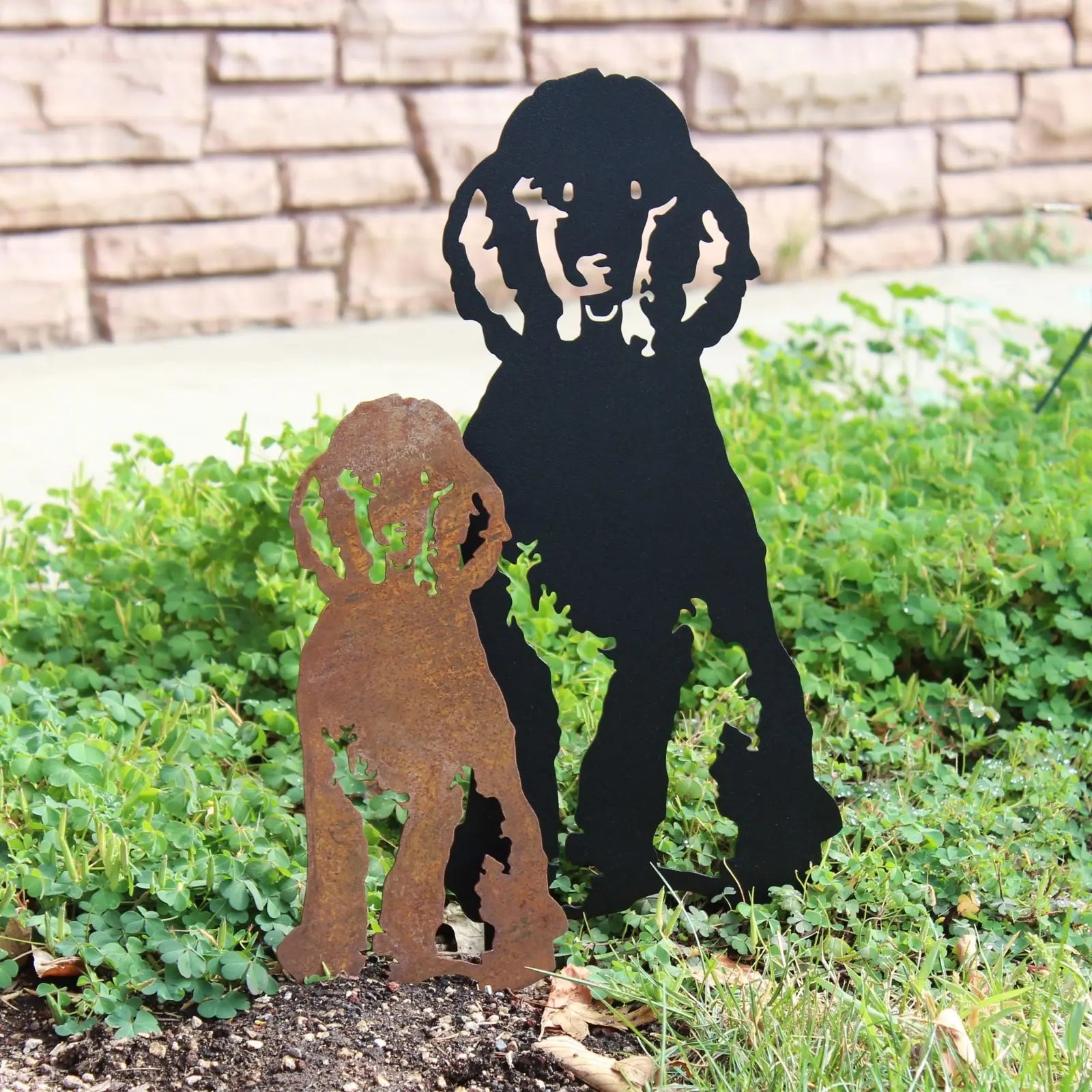 Handmade metal silhouettes of a poodle in rusted Corten steel and sleek black, set among green foliage.