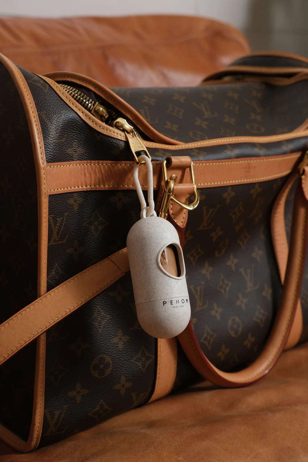 Biodegradable poop dispenser by pehomnyc, attached to a stylish leather bag, emphasizing convenience for dog owners.