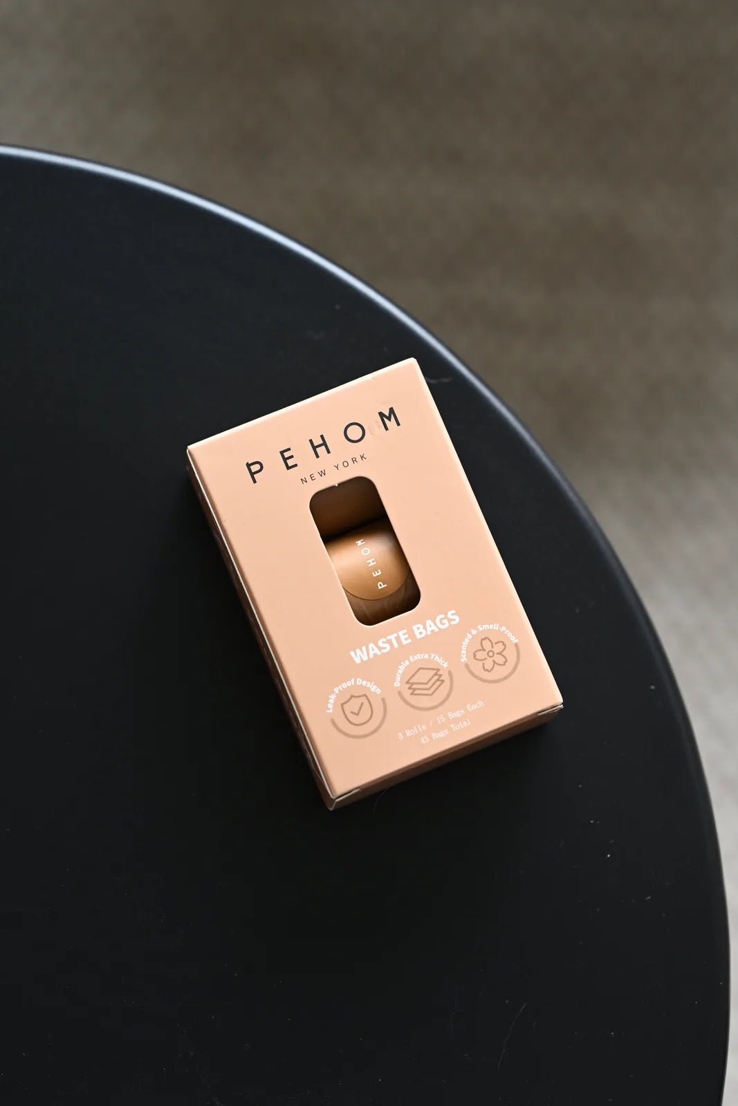 Pehom NYC waste bags in a sleek tan box, featuring a window, placed on a black surface.
